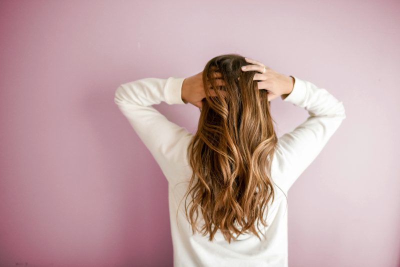 Woman experiencing menopause hair changes, standing with her back to the camera, hands in her hair.