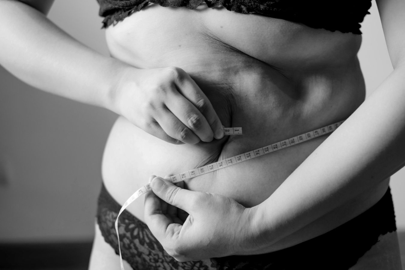 Woman measuring her waist with a tape measure during menopause, focusing on belly fat, weight gain, and healthy midlife hormone changes.