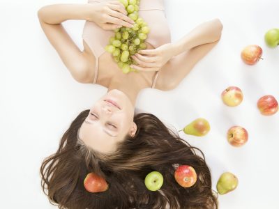 Relaxed woman lying down with fresh fruit on her body – representing holistic nutrition for perimenopause wellness