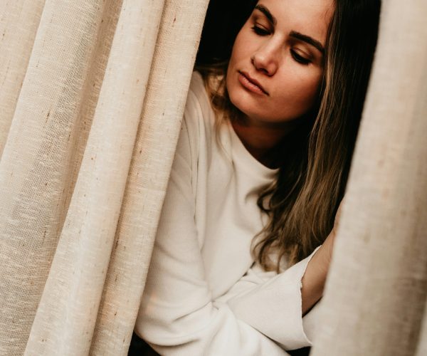 Woman sitting on a bed looking sad and emotional, reflecting depression, low mood, and emotional changes during perimenopause and menopause.
