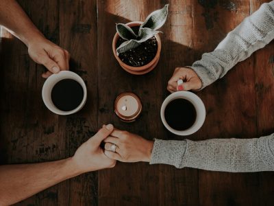 Women supporting each other during menopause treatment, holding hands across a table while sharing coffee and conversation.